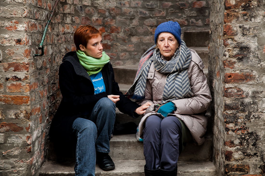 Ältere Frau sitzt mit Diakonie-Mitarbeiterin auf einer Stiege